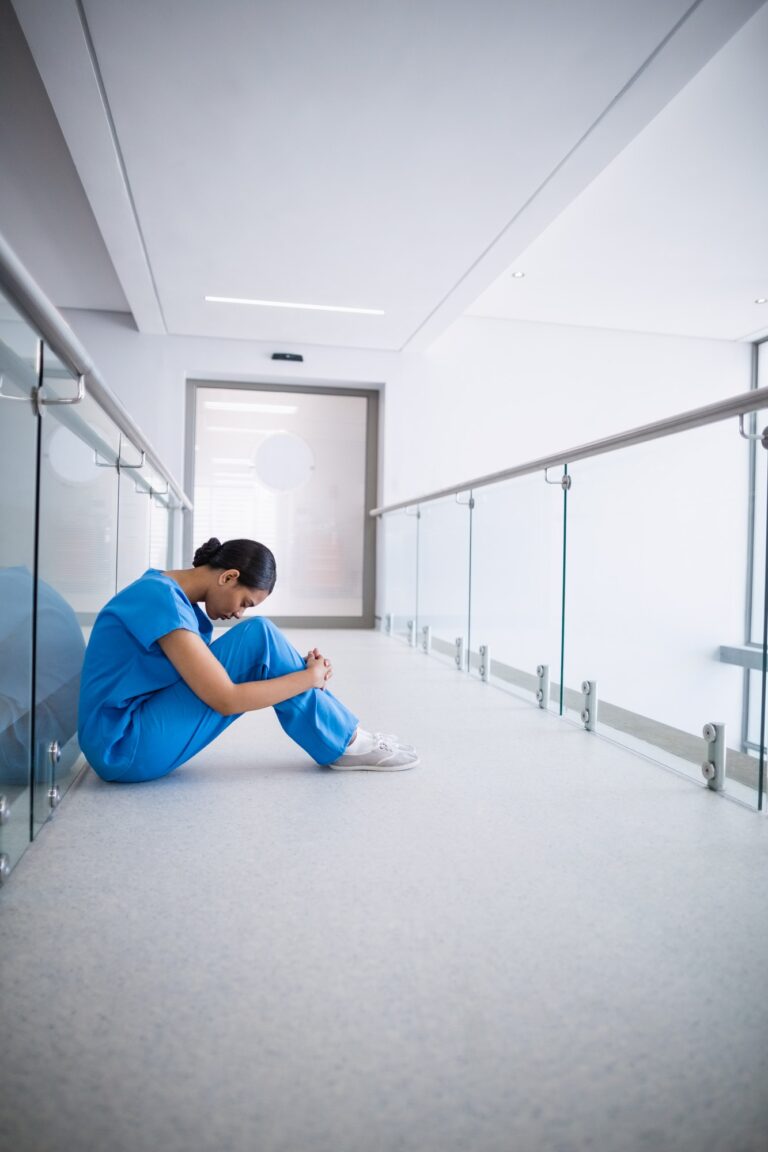 Sad nurse sitting on floor in corridor
